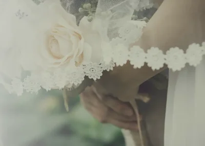 Mani di sposi unite con bouquet floreale e velo da sposa