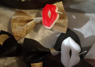 Bomboniere in fiocchi neri e dorati con candele a forma di labbra rosse e bianche, personalizzate con i 60 anni di Antonella