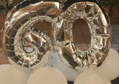 Grandi palloncini argentati a forma del numero 60, posizionati sopra palloncini sferici bianchi luminosi