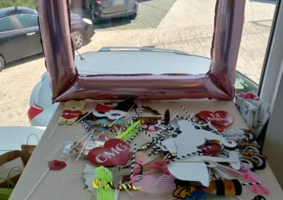 Tavolo con accessori per un photo booth, inclusi occhiali di plastica, baffi finti, cappelli, cuori e un grande cornice gonfiabile rosa