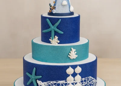 Torta a quattro piani decorata a tema marino, con colori blu e azzurri, un faro in cima, stelle marine e reti da pesca