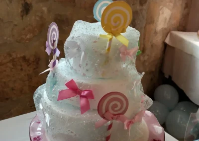 Torta scenografica a più piani, a tema lecca lecca e caramelle, decorata con tulle azzurro e rosa
