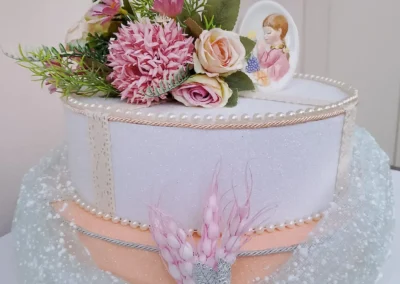 Torta decorativa a più piani per una cerimonia, con dettagli di perline, tulle e fiori finti, e una piccola immagine di una bambina per la prima comunione
