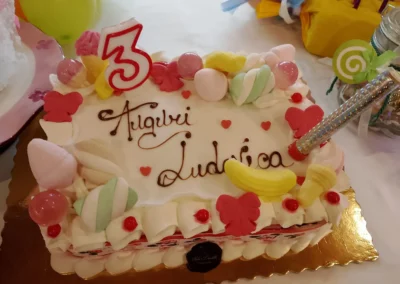 Torta di compleanno per una bambina di 3 anni, con la scritta "Auguri Ludovica", decorazioni di caramelle, marshmallow e cuori rossi