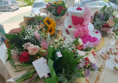 Torta a più piani con decorazioni rosa e fucsia su un tavolo circondato da grandi bouquet di fiori e oggetti di scena per foto